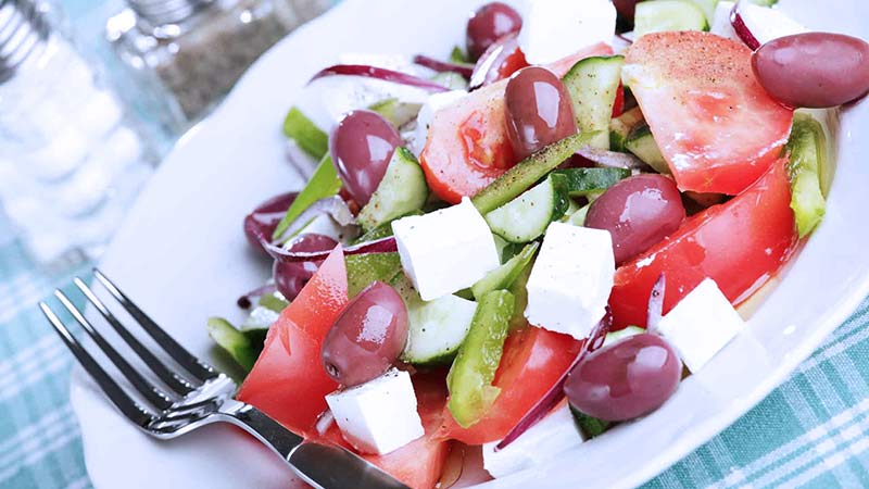 Eensalada griega con aceitunas rojas, queso feta, tomate en rodajas, pepino, pimiento y cebolla morada 