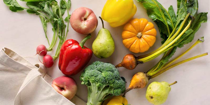 varias verduras y frutas sobre una mesa blanca y una bolsa