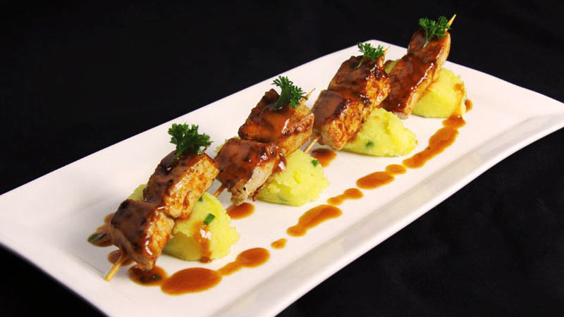 bandeja blanca con cuatro pinchos sobre un puré de patata