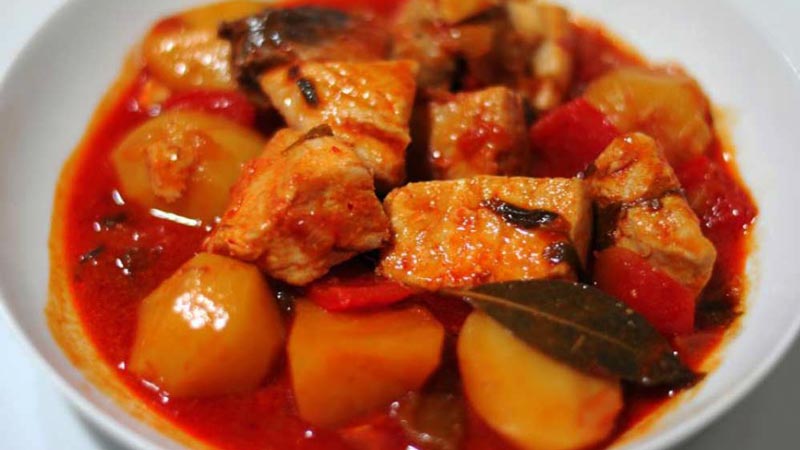 un plato blanco con carne, patatas y pimentón