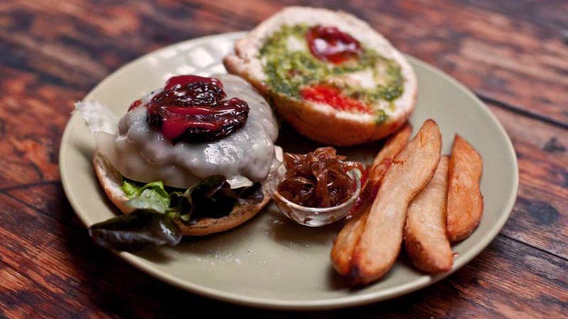 una hamburguesa abierta con varias patatas delante en un plato verde