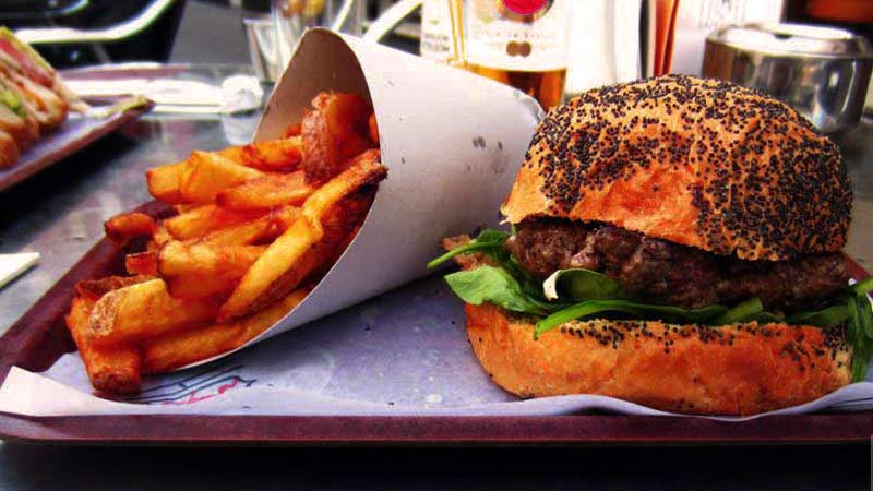 una hamburguesa con muchas semillas en el pan y con unas patatas fritas al lado