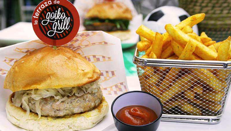 una hamburguesa con un cartel pinchado y una patatas fritas en una cesta metálica