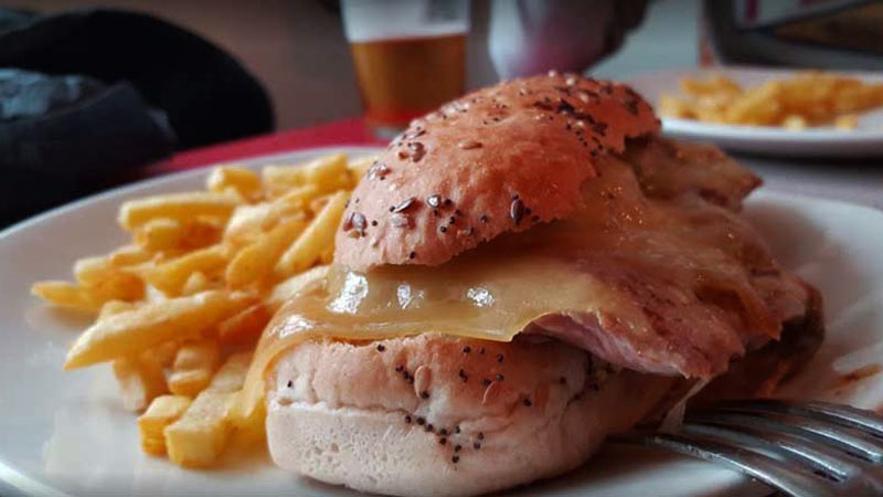 una hamburguesa con bastante queso y con patatas fritas en la izquierda