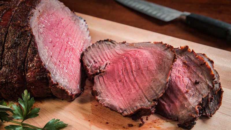 un redondo de carne con un par de trozos cortado al lado y sobre una tabla de madera