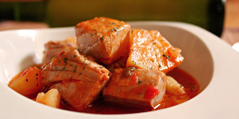 plato blanco con una receta de bonito cortado en cuadrados que está en salsa roja