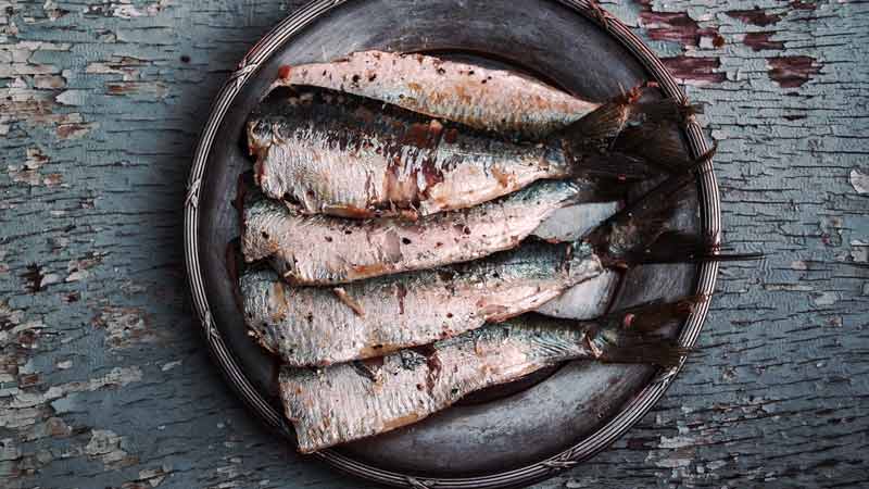 un plato con cinco sardinas sin cabeza que está encima de una mesa de madera azul