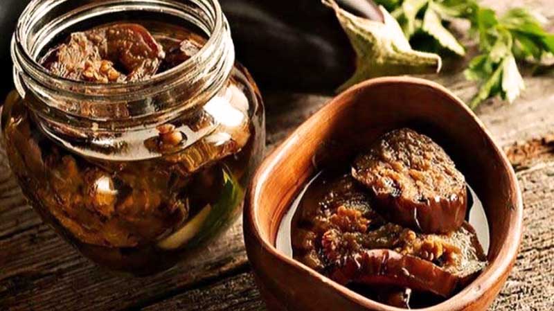 bol de madera con berenjena en aceite y que tiene al lado un tarro con más cantidad