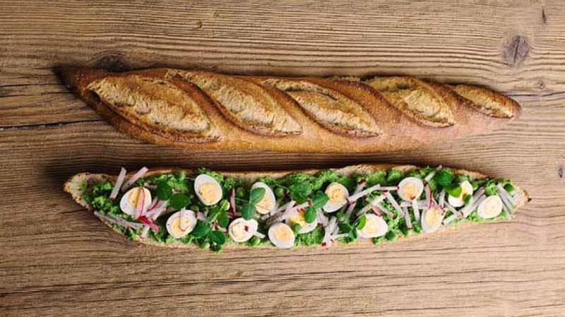 un pan cortado por la mitad, y una de esas mitades tiene hojas, cebolla y huevos cocidos