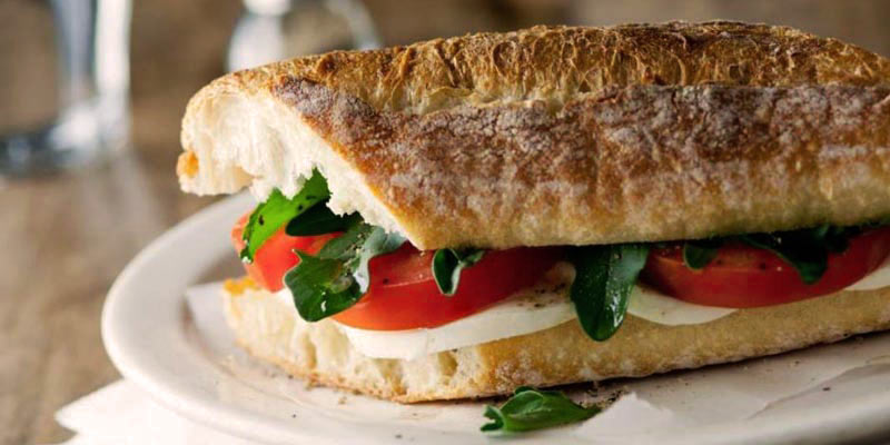 bocadillo con hojas, tomate y queso sobre un plato blanco