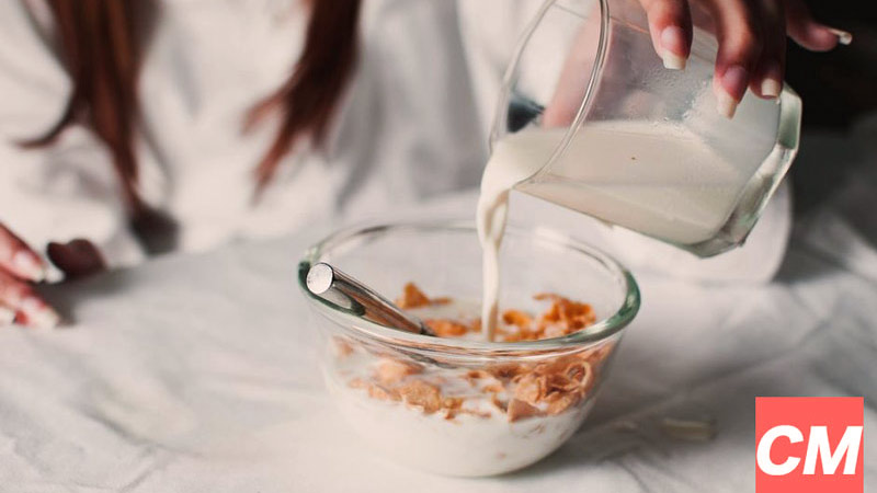 una personas volcando un vaso con leche sobre un bol con cereales