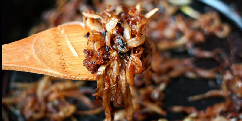 una cuchara de madera con cebolla caramelizada y debajo más en una sartén