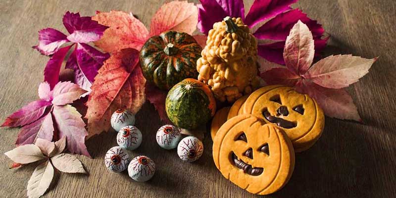 galletas con forma de calabaza con otras al lado de decoración y hojas de colores