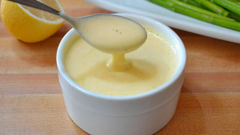 bol blanco con salsa amarilla con un limón y espárragos al fondo
