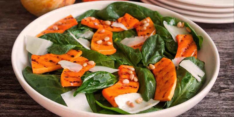 bol blanco con hojas de espinacas, frutos secos y calabaza