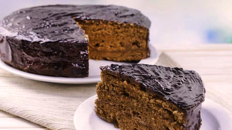 plato blanco con un pastel de chocolate que tiene un trozo cortado cobre otro plato al lado
