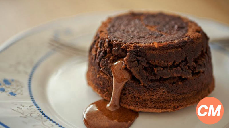 un plato redondo con decoraciones azules que tiene un bizcocho redondo del que sale chocolate líquido