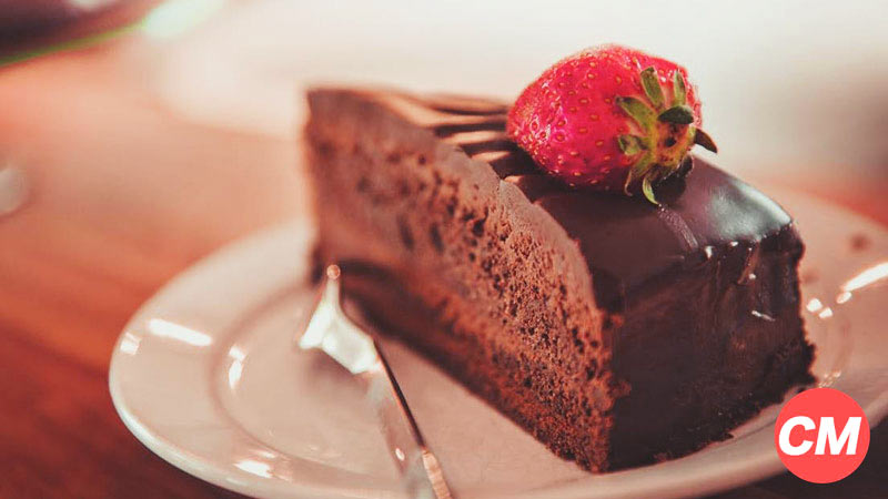 un plato blanco con una porción de pastel de chocolate con una fresa encima