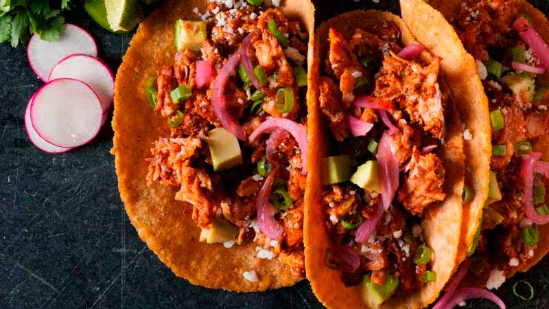 tres panes con relleno de carne, verdura y cebolla morada que están sobre una superficie negra