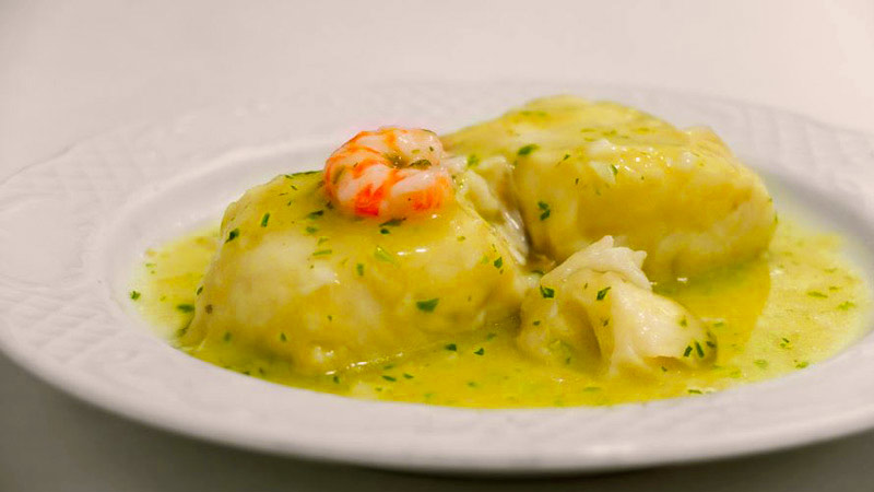 plato blanco con dos filetes de merluza con salsa y con una ganga pelada encima