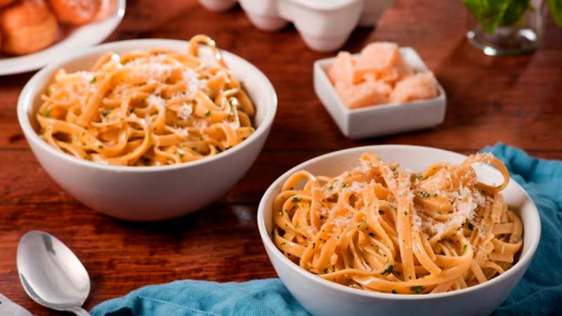 dos boles blancos con espaguetis con quesos y rodeado una cuchara, un mantel azul y otros recipientes