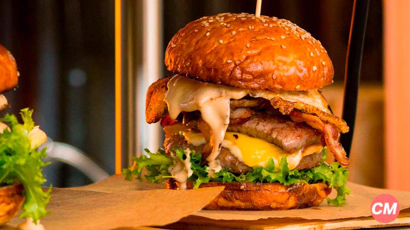 una hamburguesa con mucha carne y queso pinchada con un palo y sobre un papel