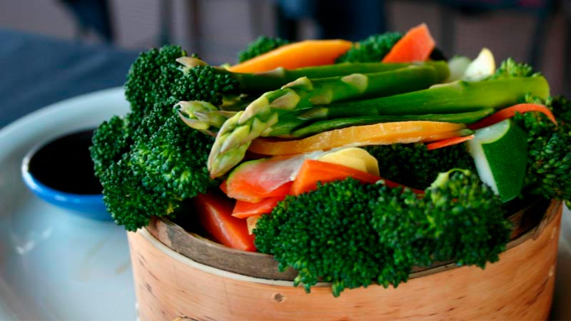 recipiente de madera circular con verduras como espárragos, zanahorias y brócoli