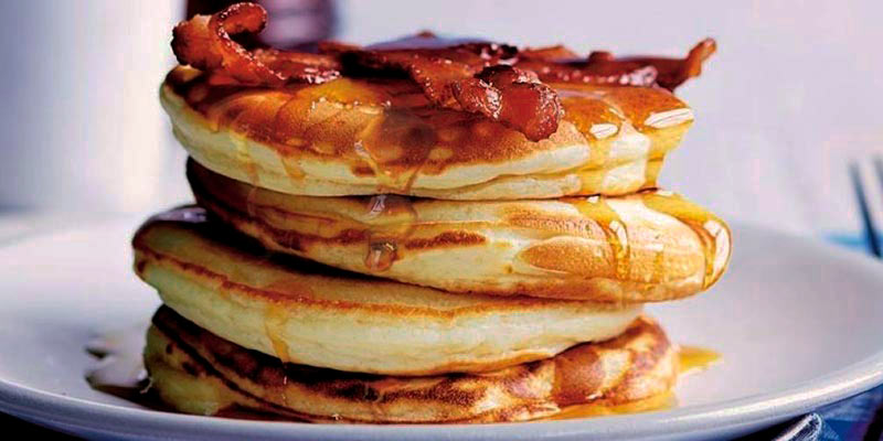 plato blanco con cuatro tortitas gruesas con bacon y sirope