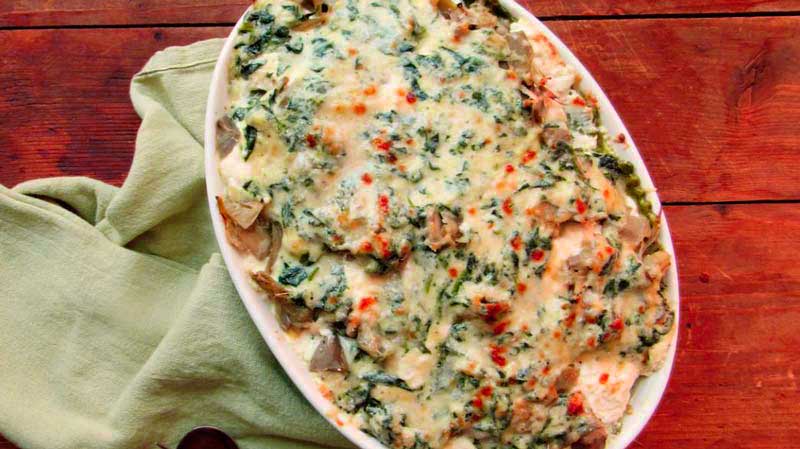 una bandeja ovalada blanca con espinacas mezcladas con bechamel que está sobre un mantel verde y, a su vez, sobre una mesa de madera