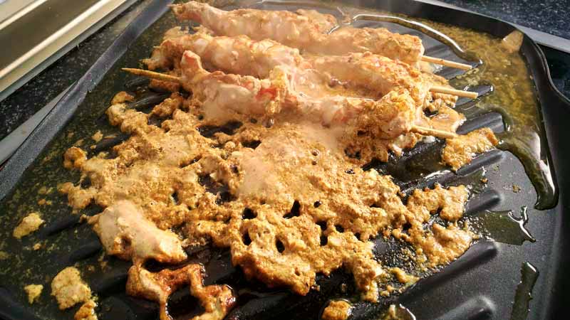 una plancha con aceite y con langostinos con pinchos sobre los cuales hay salsa
