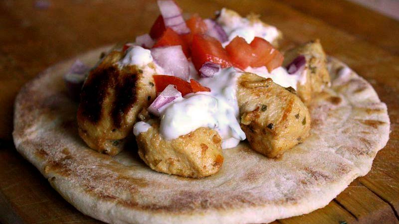 una masa de pan de pita aplanada que tiene encima piezas de carne con salsa y pimiento rojo y cebolla morada