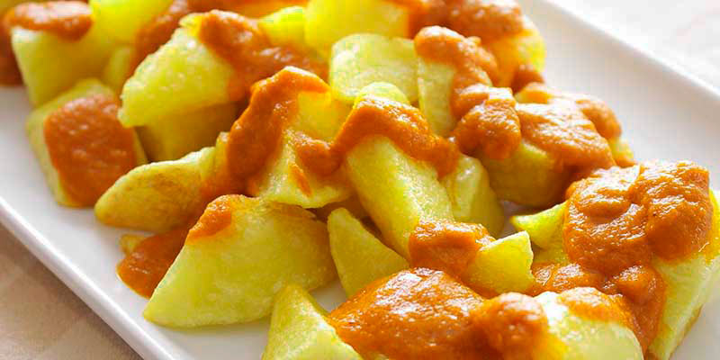 plato blanco rectangular con patatas con salsa brava por encima