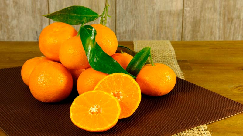 varias naranjas con hojas sobre un mantel marrón que está sobre una mesa de madera