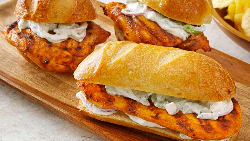 tres bocadillos pequeños con pollo y salsa sobre una tabla de madera