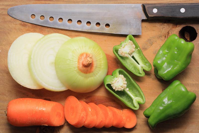 Pimienos verdes, cebolla y zanahoria troceados junto a un cuchillo.