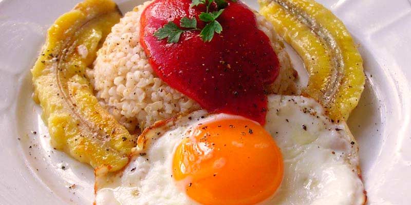 plato blanco que contiene arroz con tomate, huevo frito y plátano frito, así como también especias