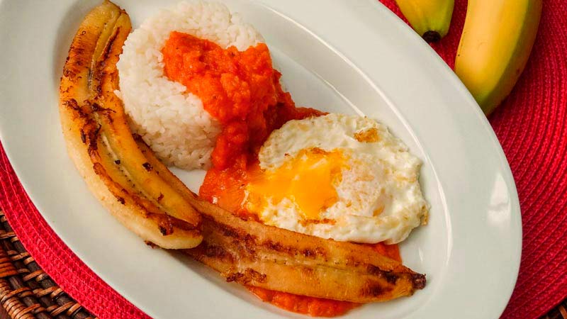 plato ovalado con arroz con tomate, huevo frito roto y plátano frito