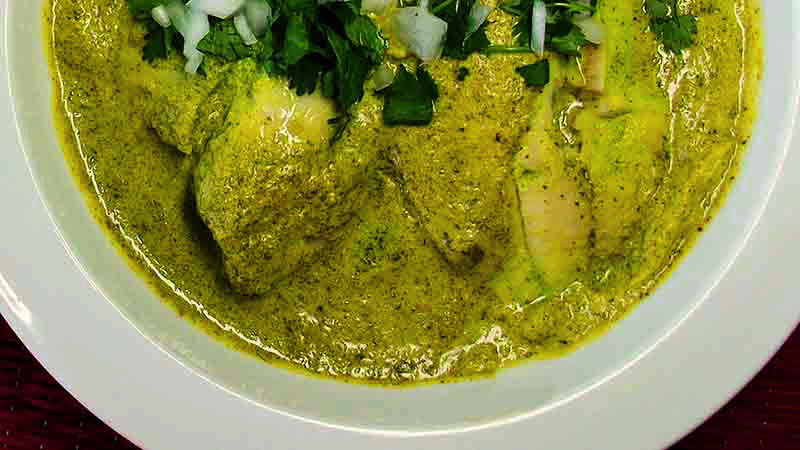 plato blanco redondo con bacalao cubierto por mucha salsa verde