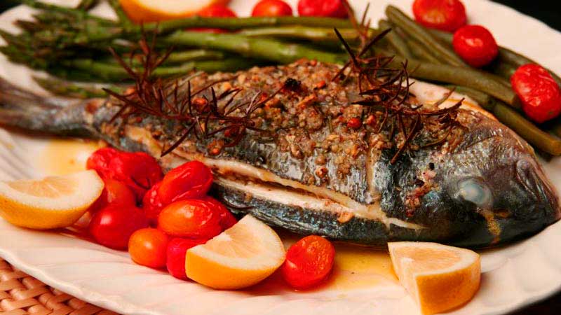 dorada sobre un plato blanco y acompañada de limón, tomate y espárragos