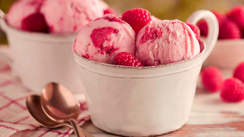 Dos recipientes blancos con varias bolas rosas de helados acompañadas de frutos rojos y dos cucharas a un lado