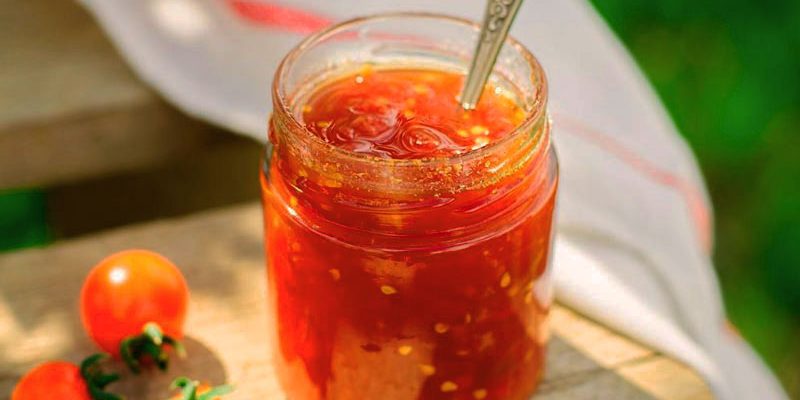 tarro de cristal con mermelada hecha de tomate y sobre una mesa de madera que tiene tomates cherry
