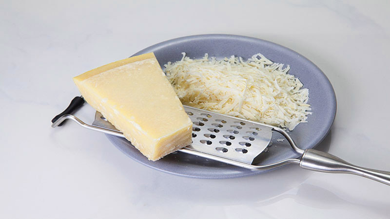 plato azul con queso rallado y que tiene un rallador y un trozo grande de queso encima