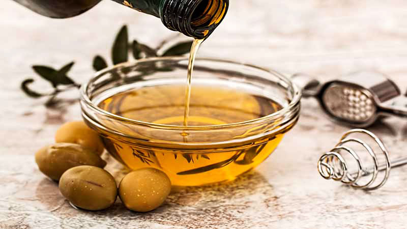bol de cristal con aceite que cae de una botella y que tiene aceitunas en la izquierda