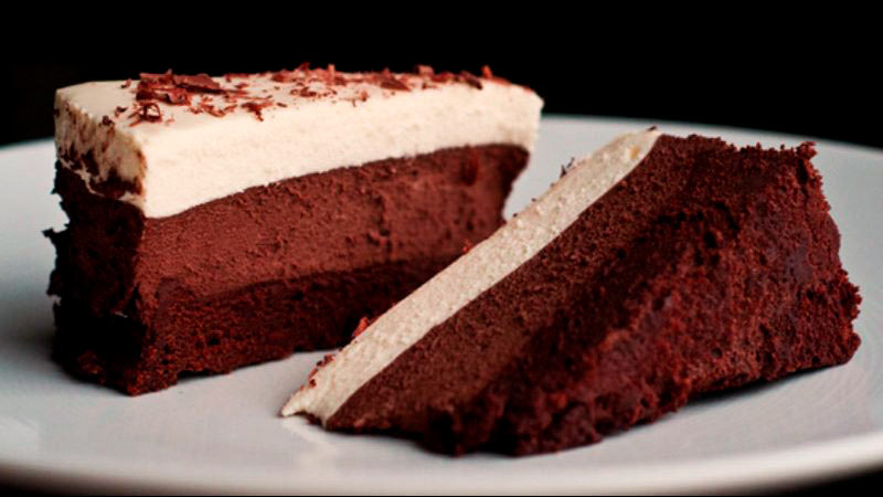 dos porciones de tarta hecha de tres chocolates sobre un plato blanco que está sobre un fondo negro