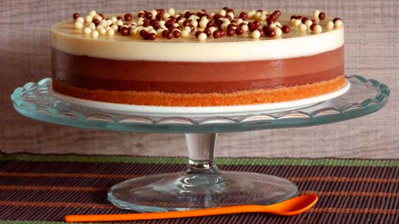 una tarta hecha de tres chocolates que está sobre una bandeja elevada sobre un mantel