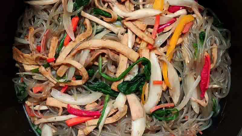 recipiente negro con fideos, carne y verduras de cortes alargados