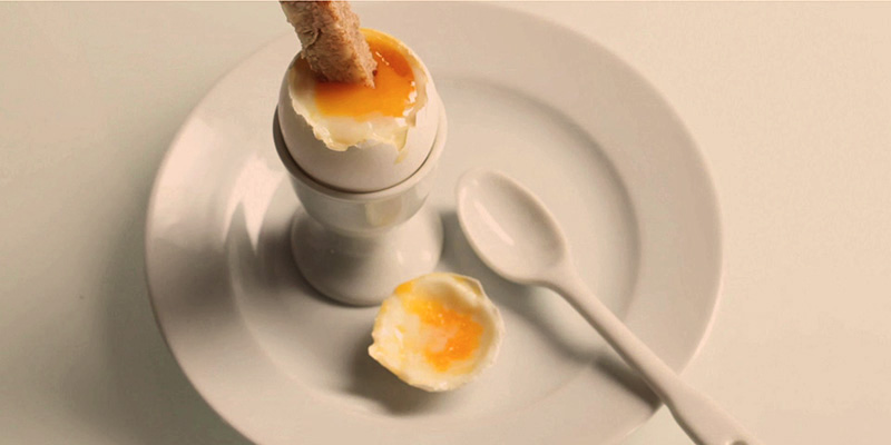 plato blanco con una cuchara blanca y un huevo roto en un recipiente también blanco