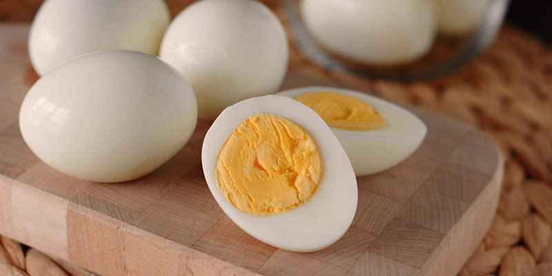 una tabla de madera con cuatro huevos cocidos encima, estando un de ellos partido por la mitad