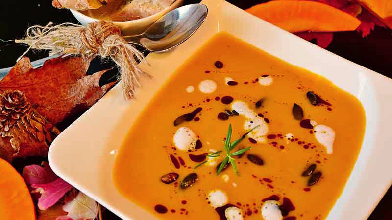 plato cuadrado con crema anaranjada que tiene semillas y que está rodeado de hojas y pétalos