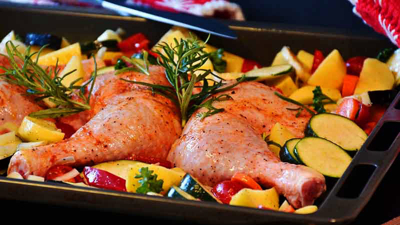 bandeja de horno con piezas de pollo y verduras aún sin cocinar